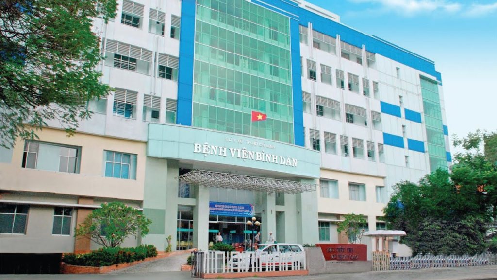 Main entrance of Binh Dan Hospital in Ho Chi Minh City, featuring a modern facade with glass panels and the Vietnamese national flag.